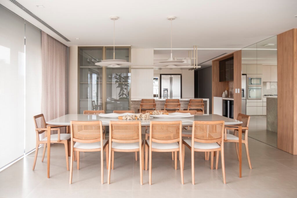 Sala de jantar com mesa ampla e dez cadeiras de madeira e pendentes com design diferenciado