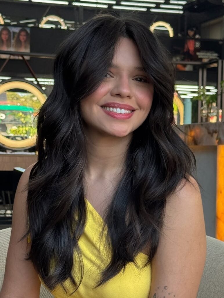 Mulher de pele clara, com blusa amarela e cabelo preto com corte shaggy hair