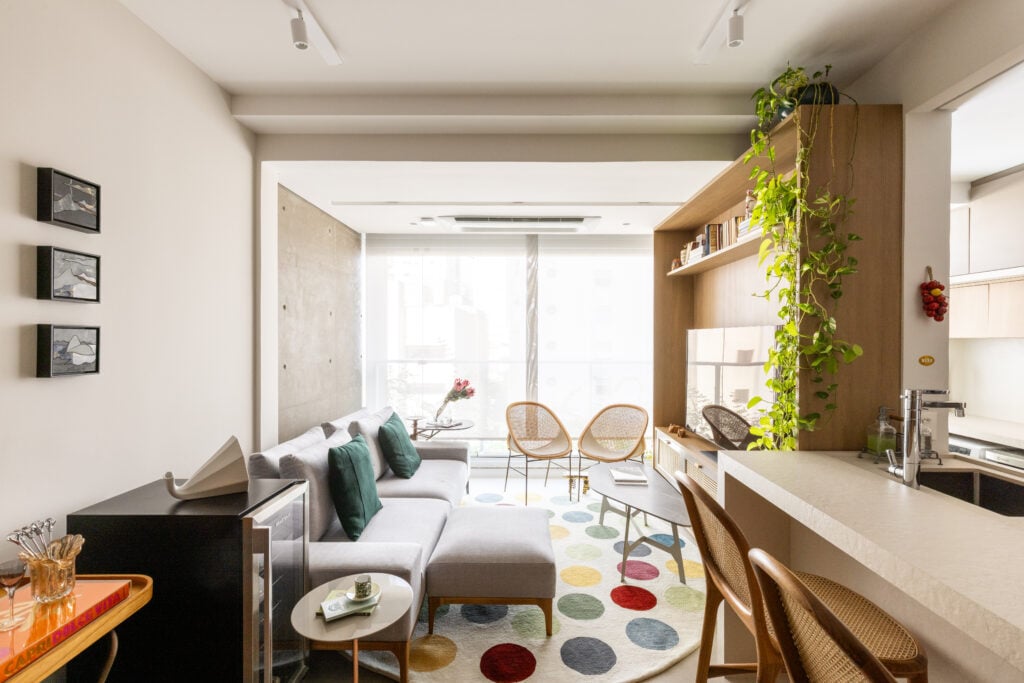Sala com iluminação natural, sofá cinza e tapete redondo com círculos coloridos