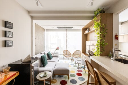 Sala com iluminação natural, sofá cinza e tapete redondo com círculos coloridos