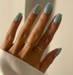 Mão de pele clara, com anéis de brilhantes e unha quadrada azul-turquesa cromada