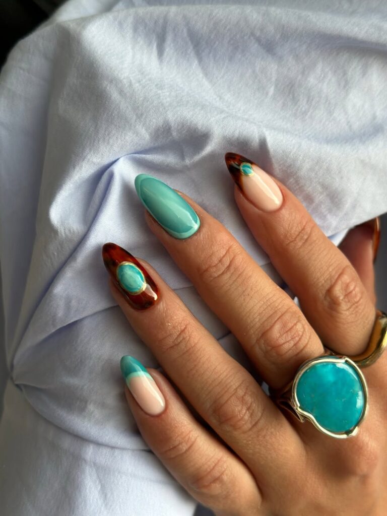 Mão de pele clara, com anéis em dourado e unha amendoada azul-turquesa com decoração de tartaruga