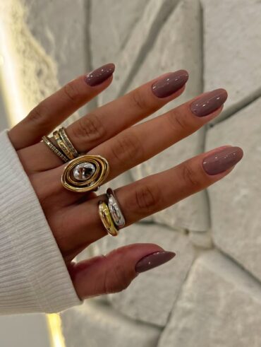 Mão de pele clara, com anéis em prata e dourado e unha amendoada nude acinzentado