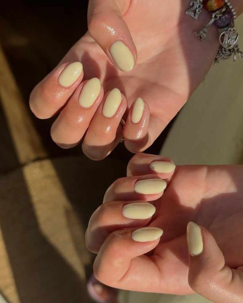 Mãos de pele clara, com unha amendoada com esmalte amarelo-manteiga