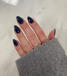 Mão de pele clara, com anéis em prata e unha amendoada azul-marinho