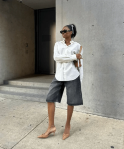 Mulher jovem e magra usando camisa branca, bermuda jeans e salto alto