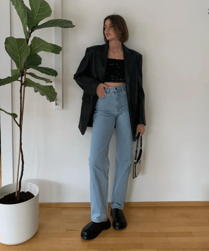 Mulher jovem e magra com blazer, calça jeans e top de paetê