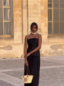 Mulher jovem e magra de pele negra. Ela usa vestido feminino preto sem alça
