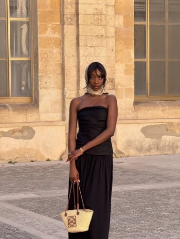 Mulher jovem e magra de pele negra. Ela usa vestido feminino preto sem alça