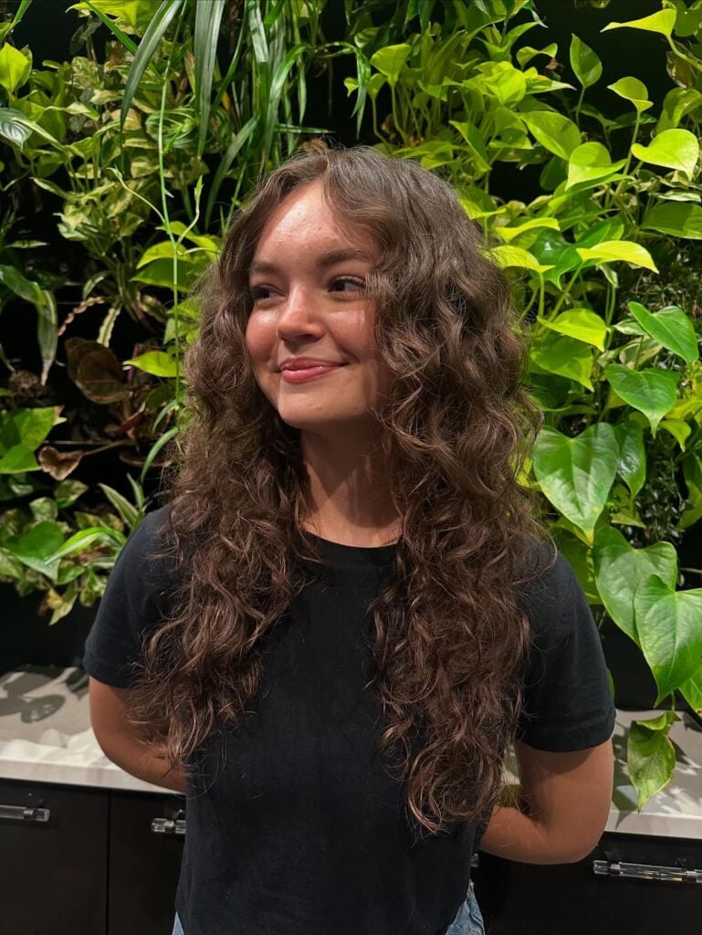 Mulher de pele clara com cabelo cacheado longo e com corte borboleta