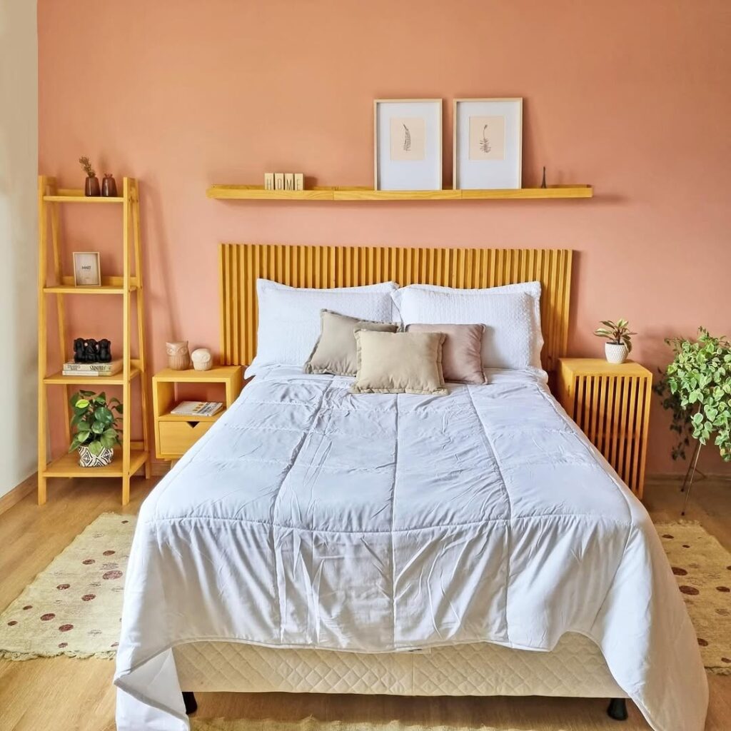 Quarto com parede rosa atrás da cama, cabeceira de madeira ripada, estante e mesas de cabeceira amadeiradas