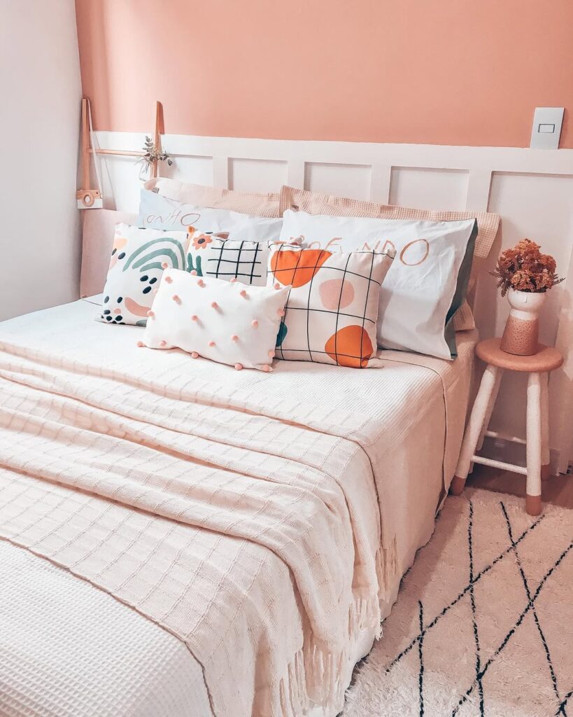 Quarto feminino com almofadas decorativas, parede rosa e cabeceira de madeira branca