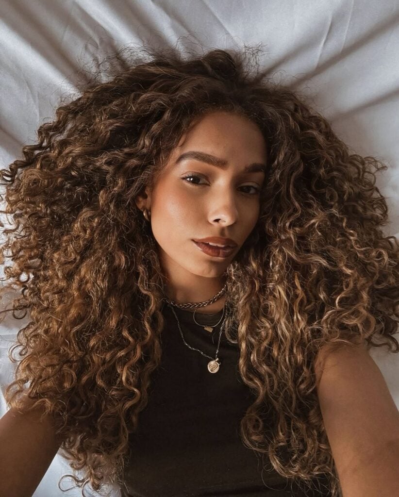 Mulher deitada com cabelo cacheado comprido loiro mel