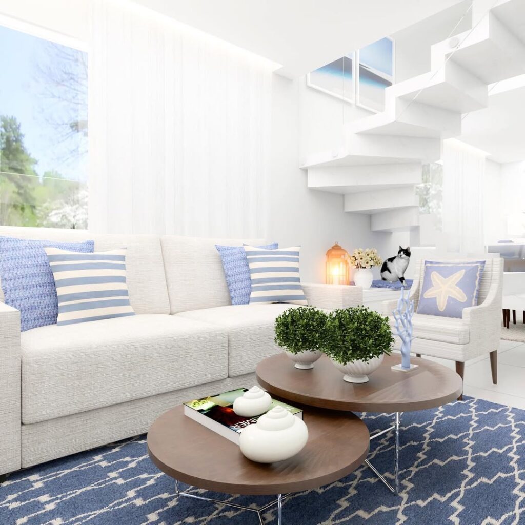 Sala de praia com sofá branco, almofadas em azul e branco e mesas de centro marrom