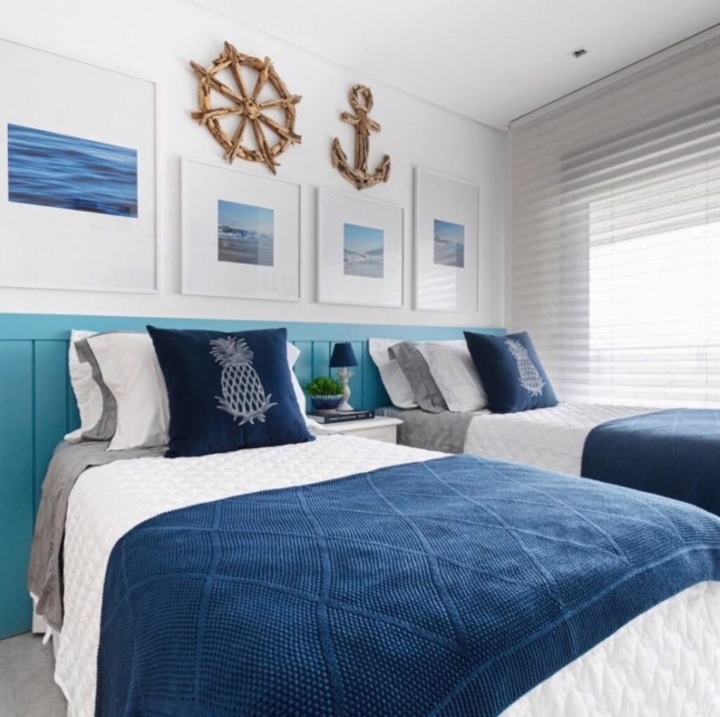 Quarto com duas camas, quadros nas cabeceiras e roupas de cama em azul e branco