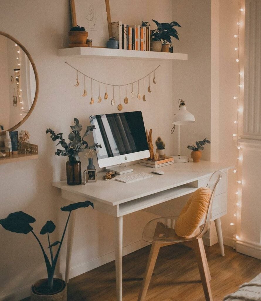 Home office com escrivaninha branca, luminária, objetos e prateleira acima