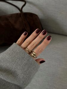 Mão de pele clara, com anéis em dourado e unha curta e redonda burgundy