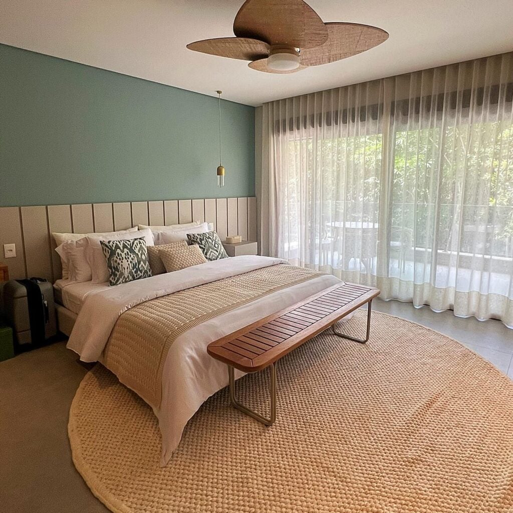 Quarto de casal com parede em tom de verde, tapete grande redondo e cortina branca