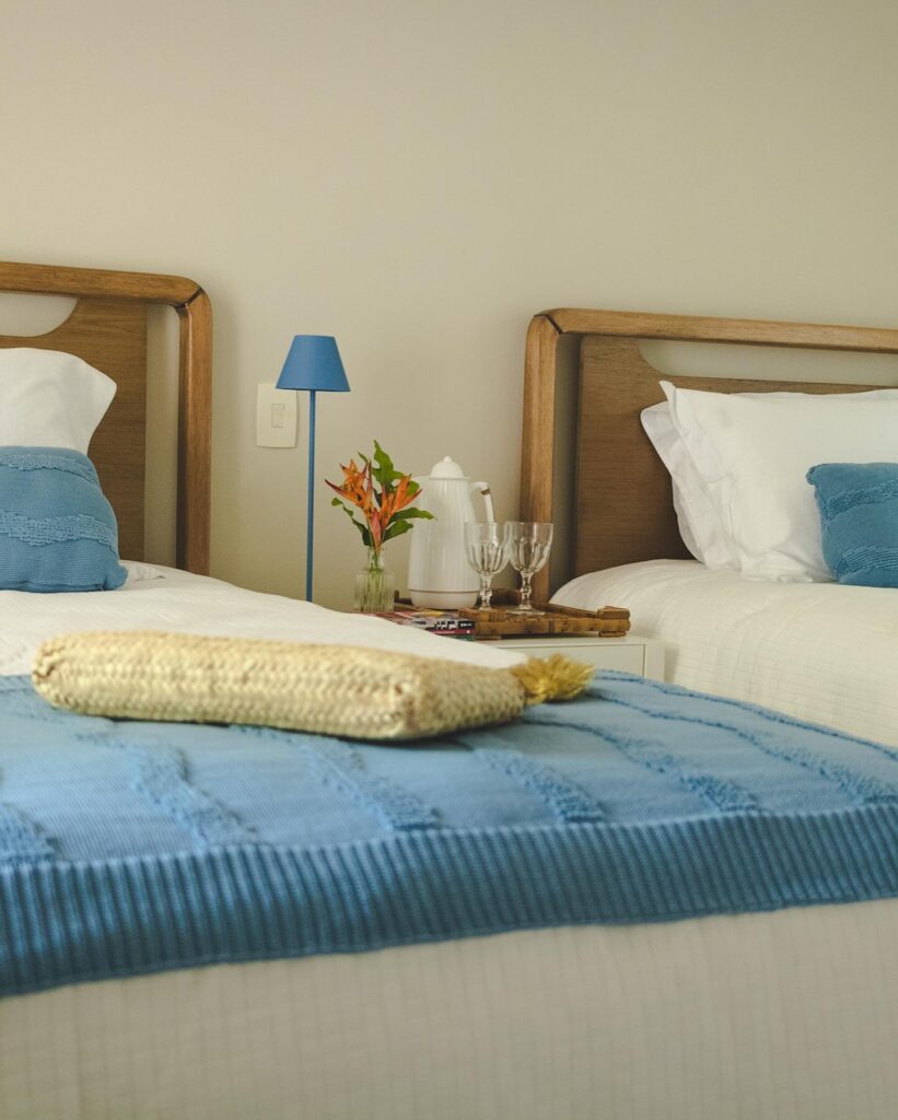 Quarto com duas camas, cabeceira de madeira, luminária e almofadas azuis
