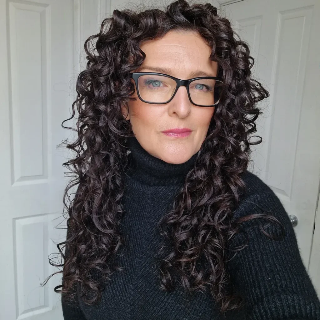 Mulher de pele clara, com tricot preto e cabelo longo cacheado com corte em camadas