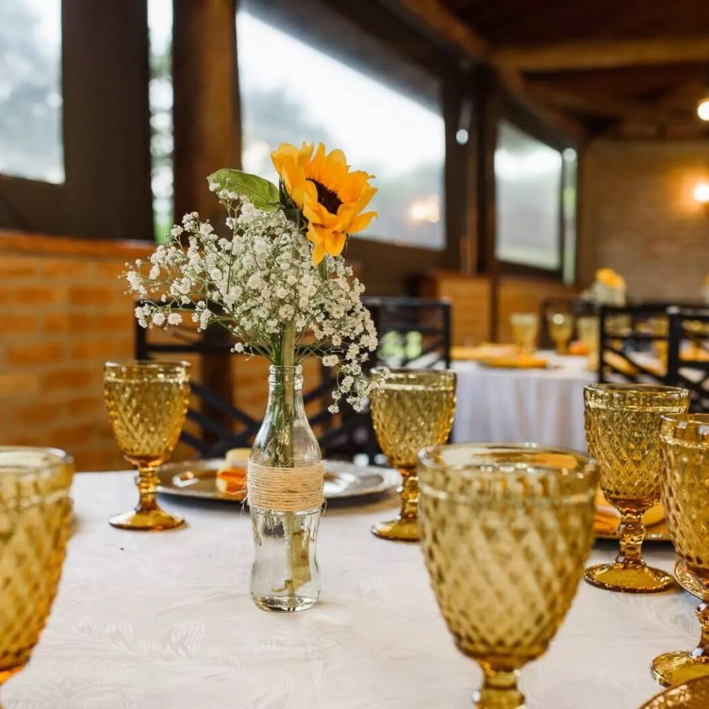 Mesa com taças amarelas e garrafa transparente com florzinhas brancas
