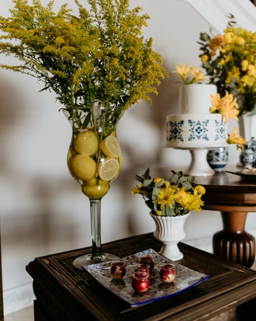 Vaso de vidro decorado com limões amarelos, vaso pequeno branco com flores amarelas