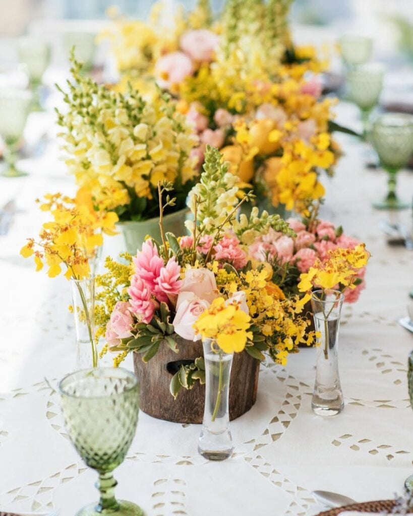 Mesa com toalha branca e arranjos com flores amarelas e rosas