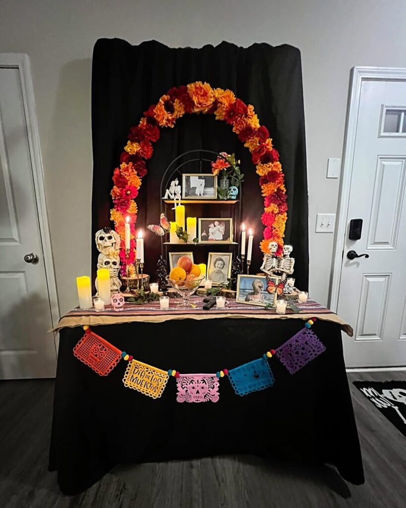 Altar montado com fundo preto, bandeirinhas coloridas, caveiras e velas
