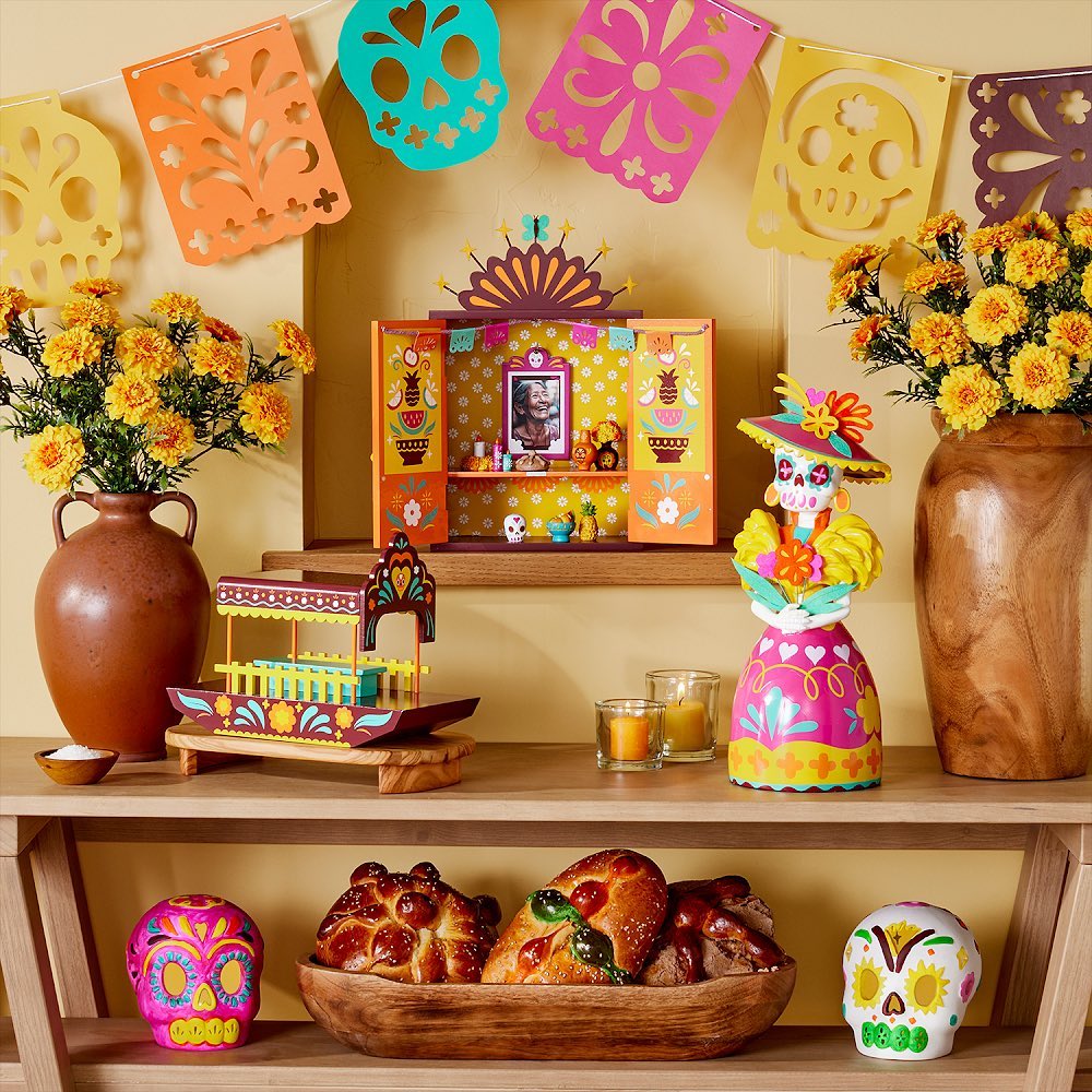 Prateleiras de madeira com vasos marrons e flores amarelas, boneca no estilo mexicana, desenhos recortados de papel