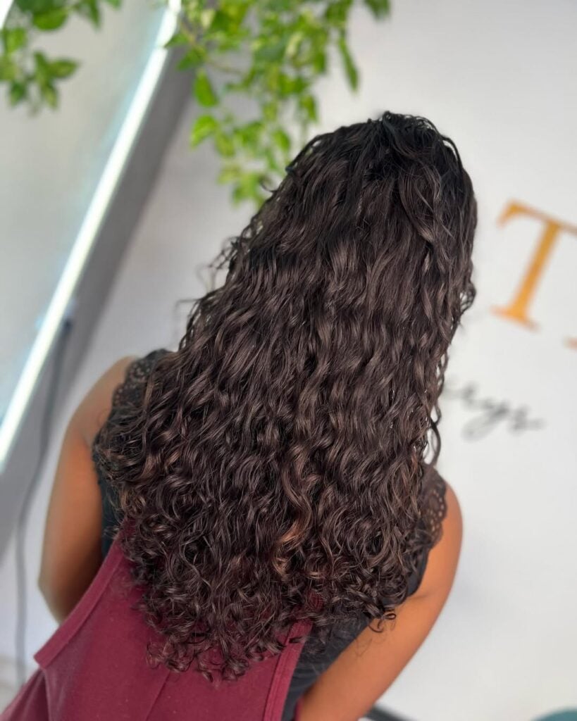 Mulher de pele preta, com cabelo longo cacheado com corte em V