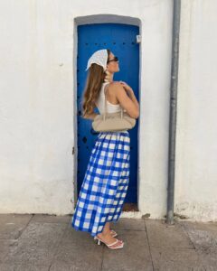Mulher de pele clara, com regata branca, saia azul xadreza kitten heels e bonet