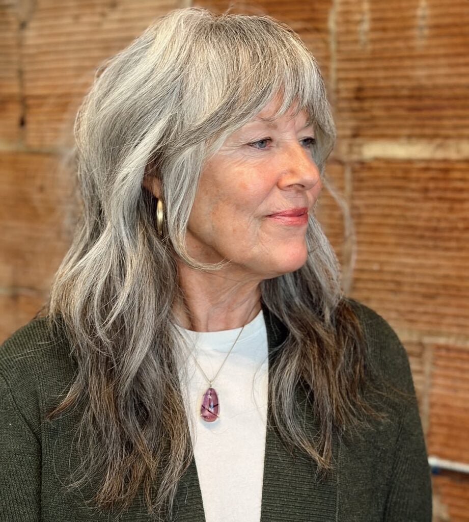 Mulher de pele clara, com acessórios em dourado e prata e cabelo grisalho com franja bardot