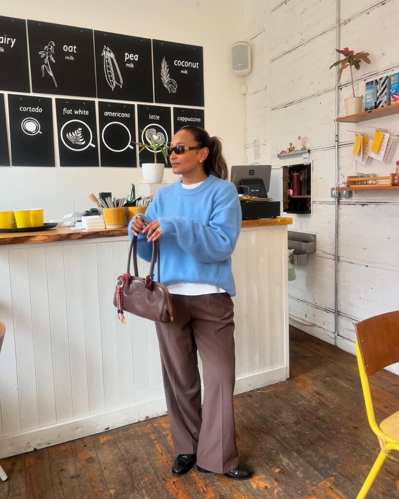 Mulher jovem com suéter azul, calça marrom e bolsa marrom