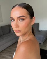 Mulher de pele clara, com acessórios em dourado e cabelo preso. Ela está com uma maquiagem clean