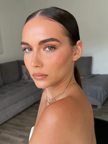 Mulher de pele clara, com acessórios em dourado e cabelo preso. Ela está com uma maquiagem clean