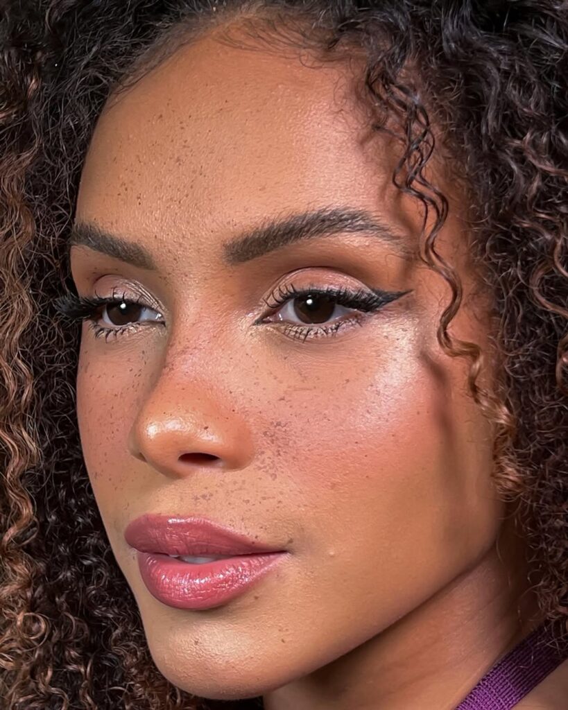 Mulher de pele preta, com cabelo cacheado e maquiagem com delineado e sardas