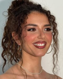 Mulher de pele negra-clara, com cabelo cacheado e maquiagem com sardas fakes