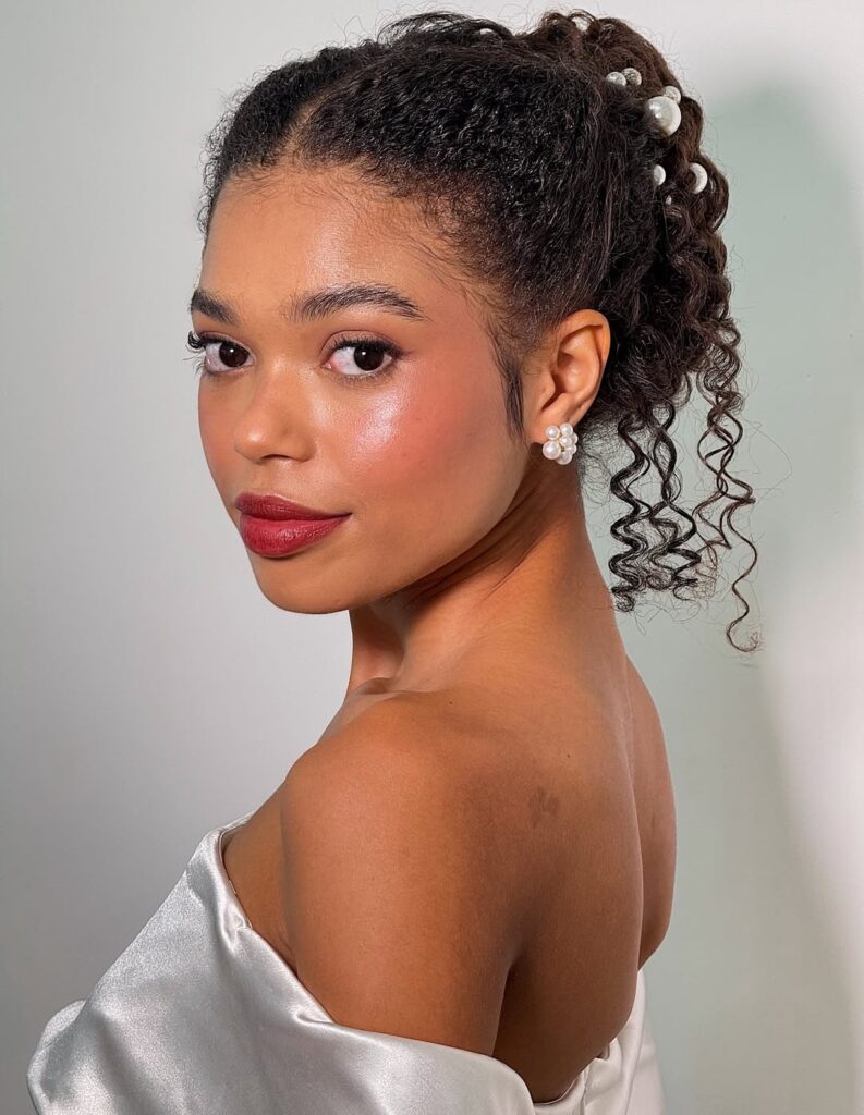 Mulher de pele preta, com vestido de noiva, cabelo crespo preso e maquiagem clean