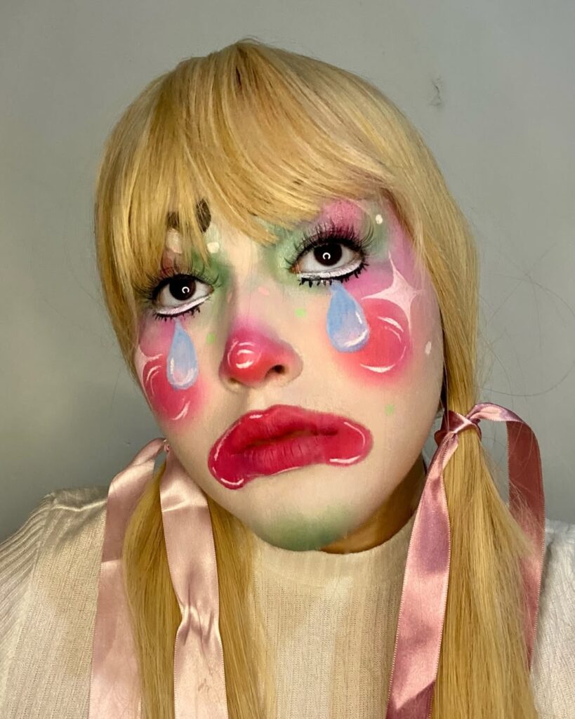 Mulher, de peruca loira, com maquiagem de palhaço colorida