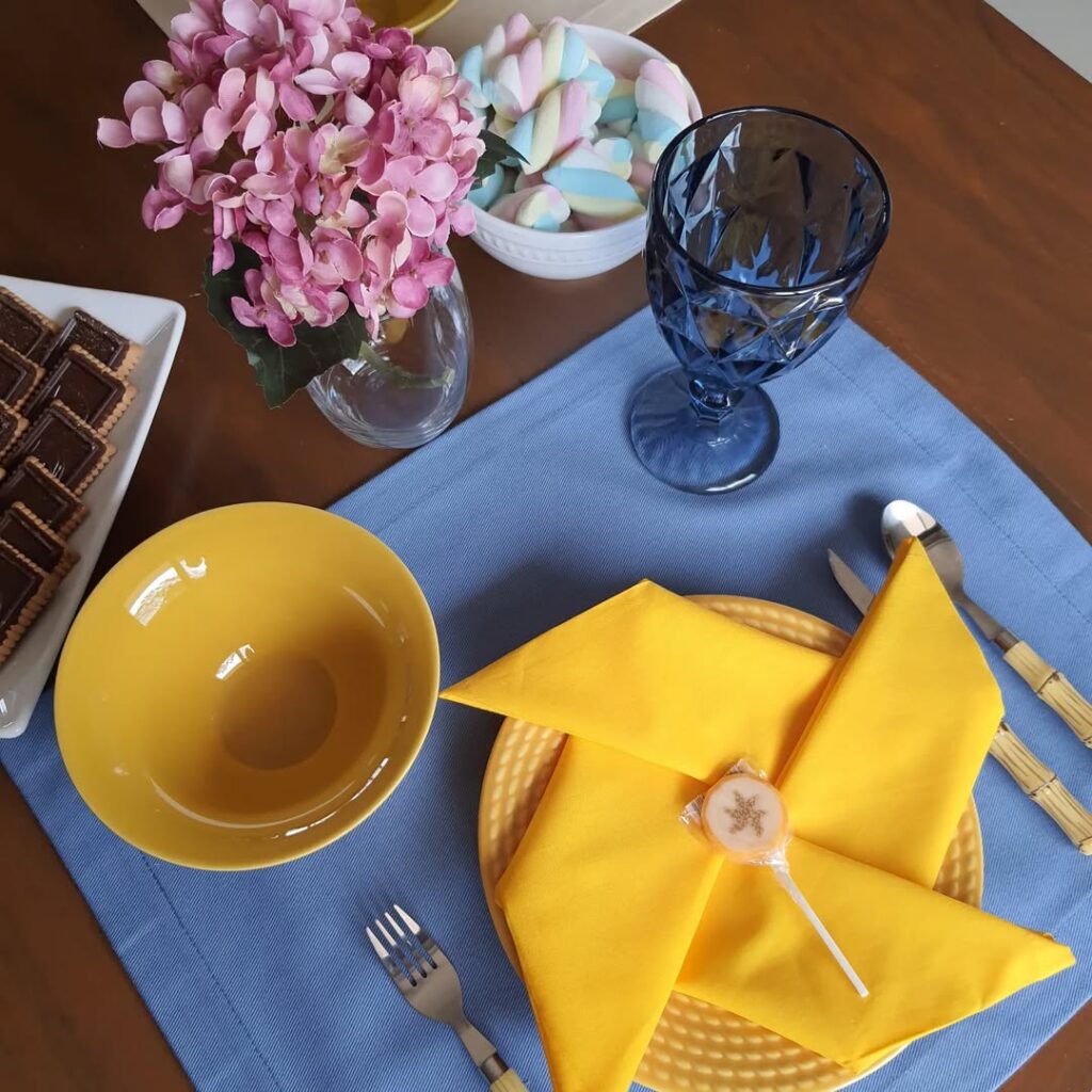 Mesa posta com jogo americano azul, pratinhos e guardanapo amarelo