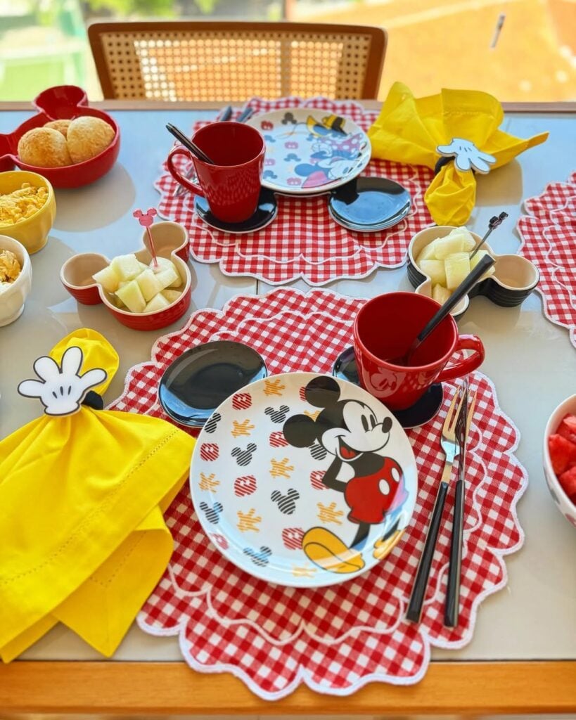 Mesa posta para o dia das crianças com jogo americano xadrez em vermelho e branco, pratos com Mickey e canecas vermelhas