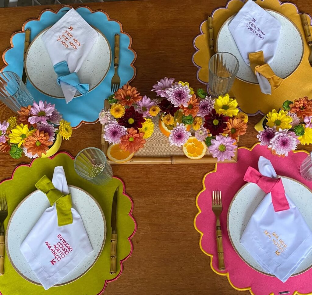 Mesa posta com sousplats coloridos e flores do campo rosas, laranja e amarelas