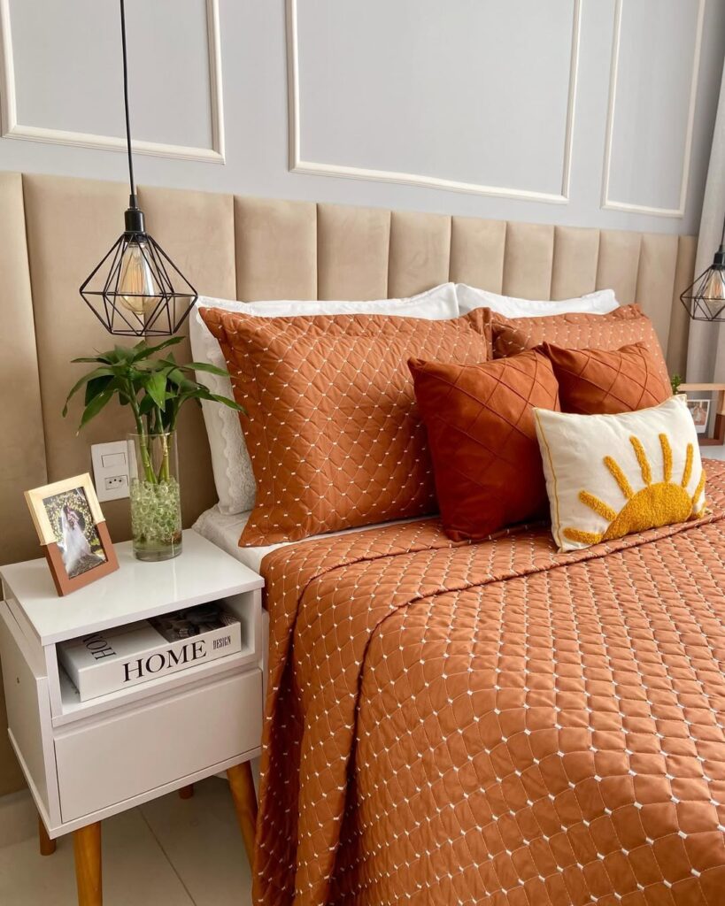 Quarto com cabeceira estofada modular, roupa de cama terracota e mesinha de cabeceira branca com pés palito