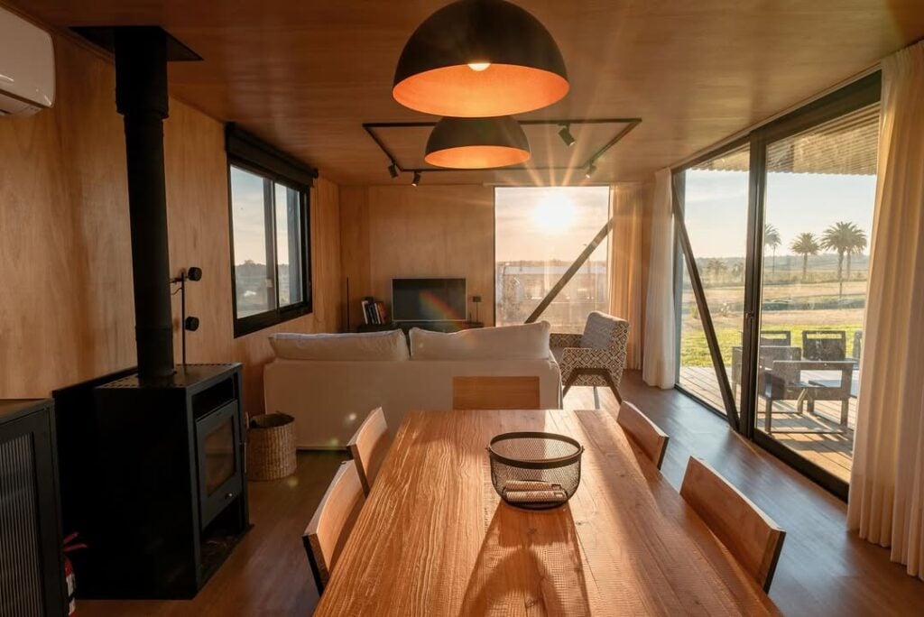 Casa modular com mesa de madeira, sofá brancos e pendentes