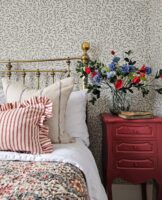 Quarto com cabeceira dourada, papel de parede em branco e azul e mesa de cabeceira com vaso de flores