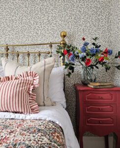 Quarto com cabeceira dourada, papel de parede em branco e azul e mesa de cabeceira com vaso de flores