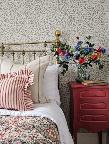 Quarto com cabeceira dourada, papel de parede em branco e azul e mesa de cabeceira com vaso de flores