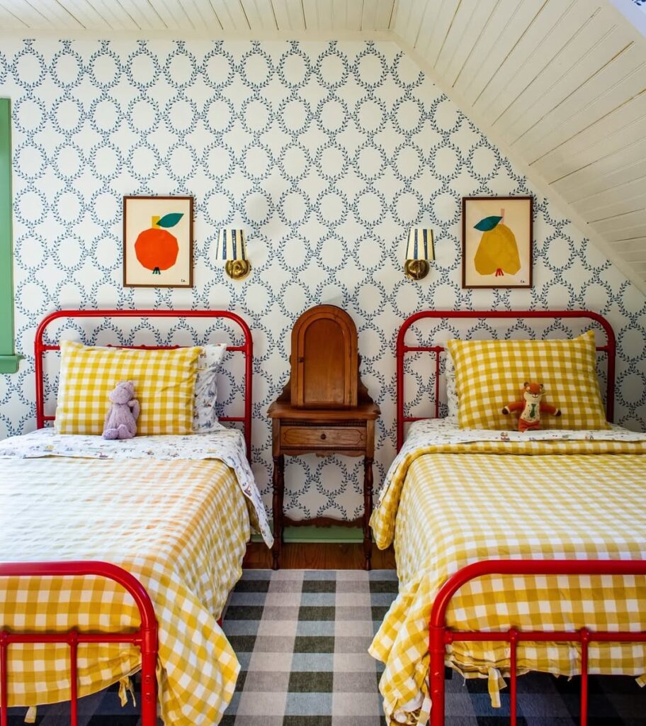 Quarto com duas camas vermelhas, colcha xadrez em branco e amarelo e papel de parede com quadros