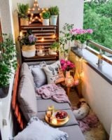 Pequena varanda de apartamento com sofá, almofadas, vasos com plantas e flores