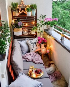 Pequena varanda de apartamento com sofá, almofadas, vasos com plantas e flores